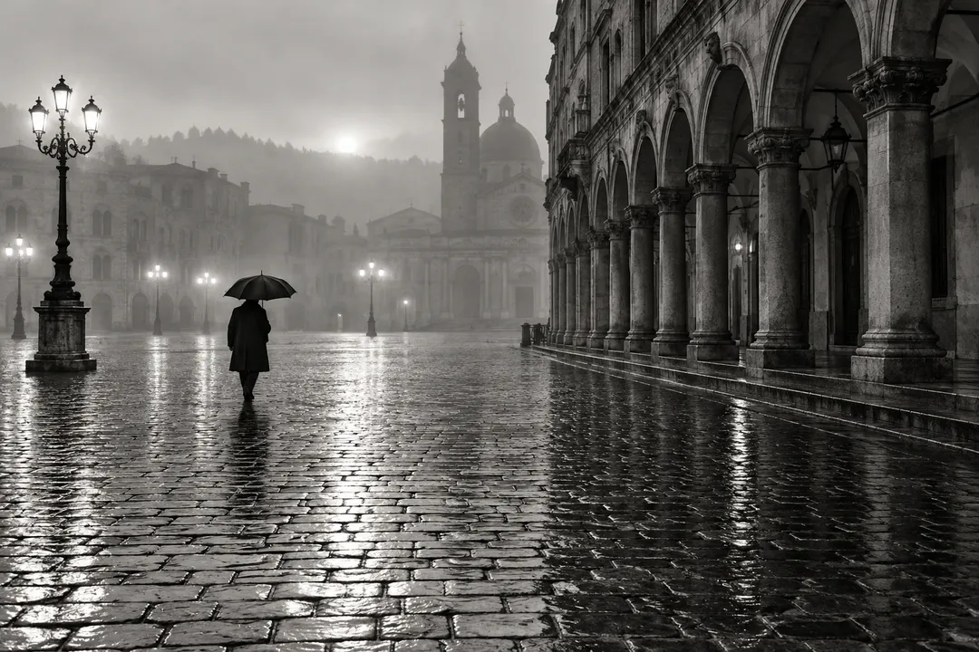 A figure with an umbrella crossing a wet cobbled square at dawn, black and white