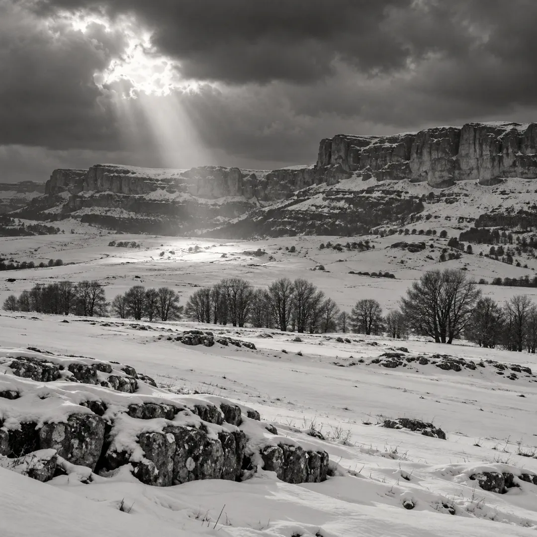 Snow on a limestone plateau under a break in the clouds, black and white